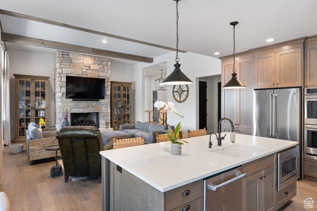 Kitchen with a sink, appliances with stainless steel finishes, open floor plan, a kitchen island with sink, and light wood-type flooring
