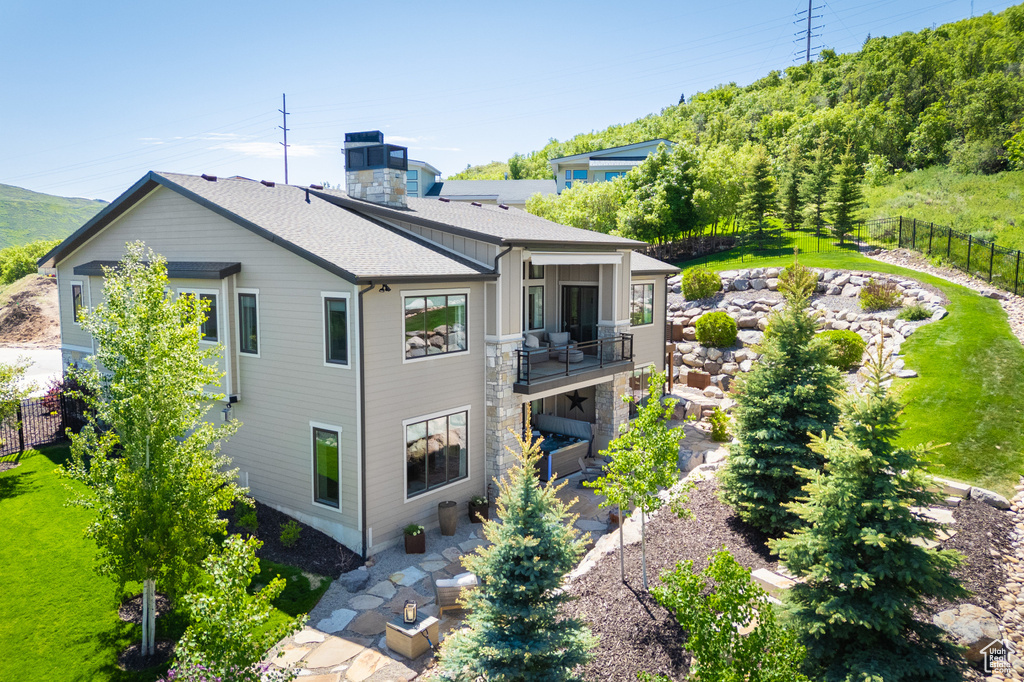 Rear view of house with a balcony, a patio, and roof with shingles