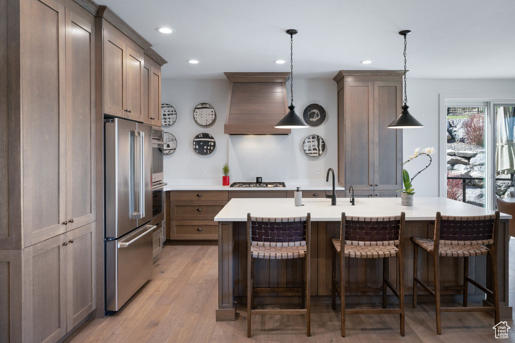 Kitchen with appliances with stainless steel finishes, premium range hood, recessed lighting, light countertops, and a sink