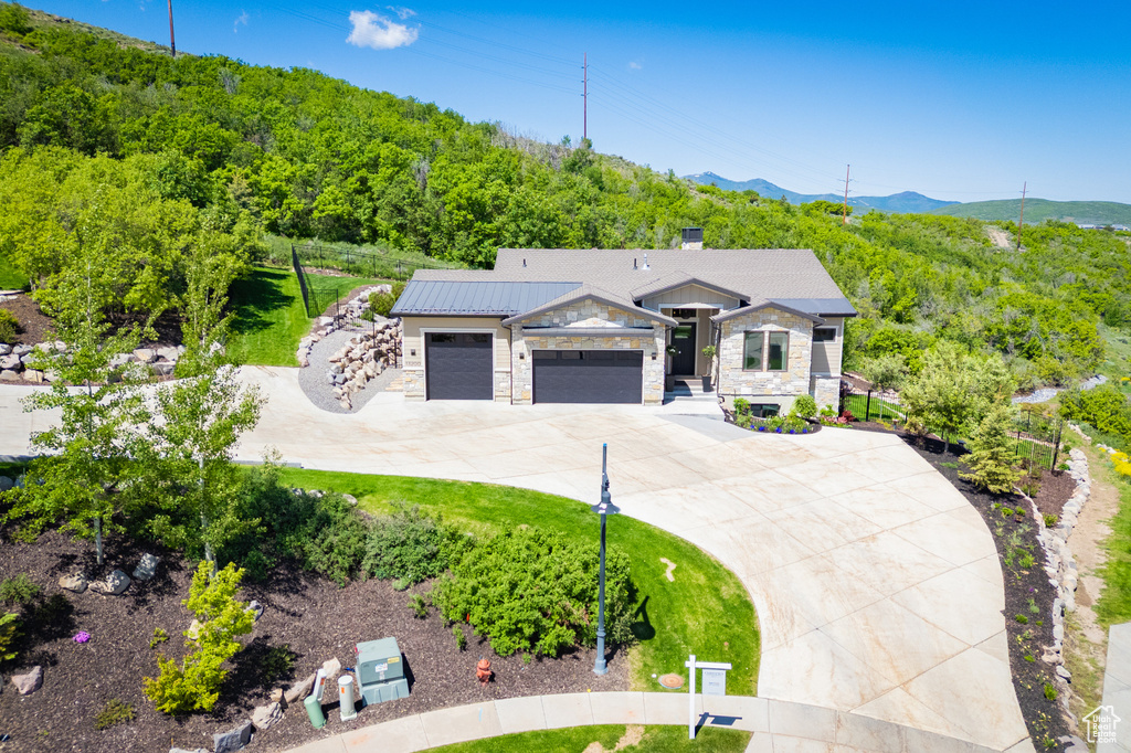 View of front of home with driveway, a garage, stone siding, a mountain view, and a chimney