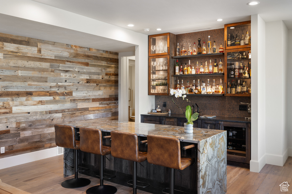Indoor wet bar featuring beverage cooler, wood walls, light wood-type flooring, recessed lighting, and decorative backsplash