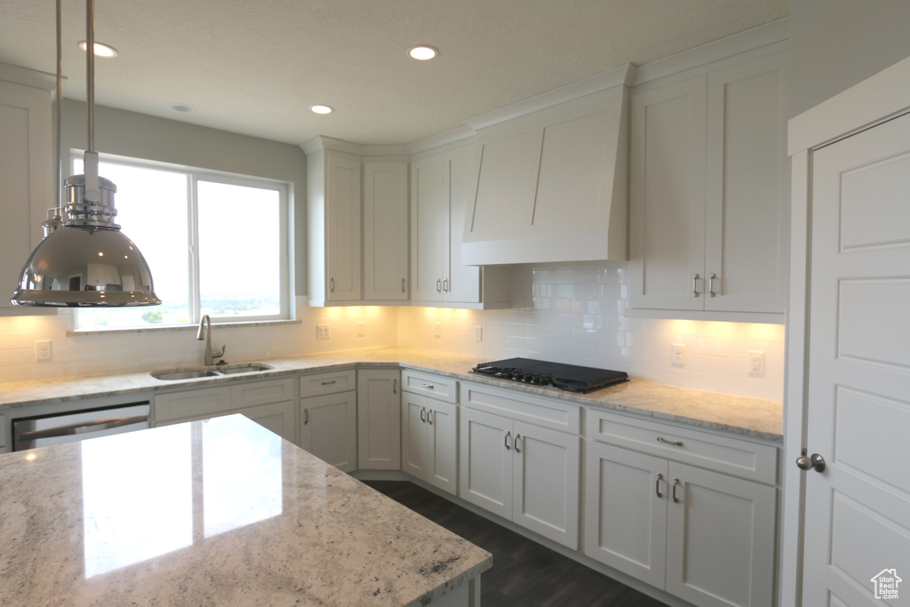 Kitchen featuring a sink, black cooktop, backsplash, exhaust hood, and stainless steel dishwasher
