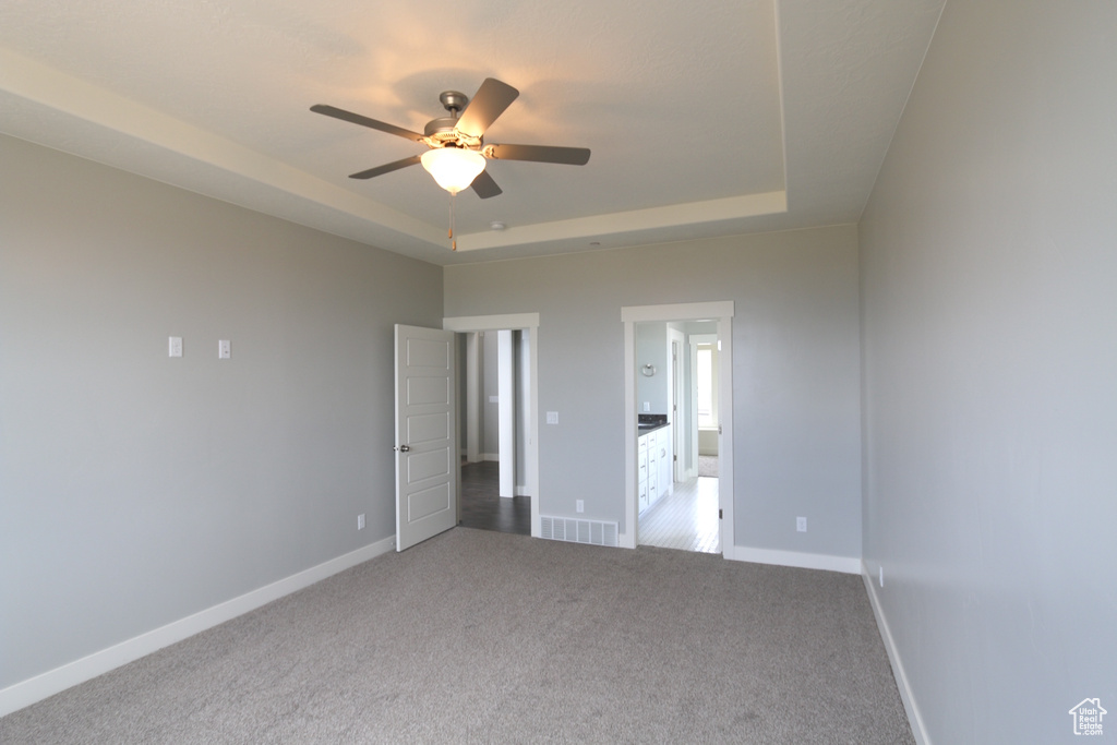 Unfurnished bedroom featuring a raised ceiling, carpet, baseboards, and ceiling fan
