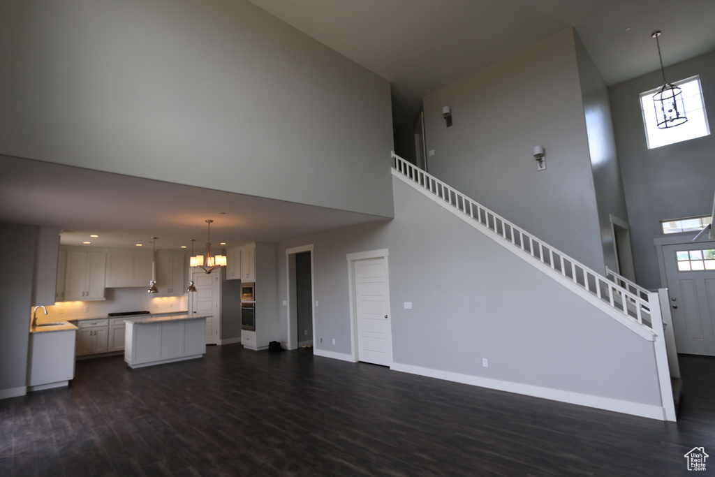 Unfurnished living room with a towering ceiling, a chandelier, a sink, dark wood-style floors, and baseboards