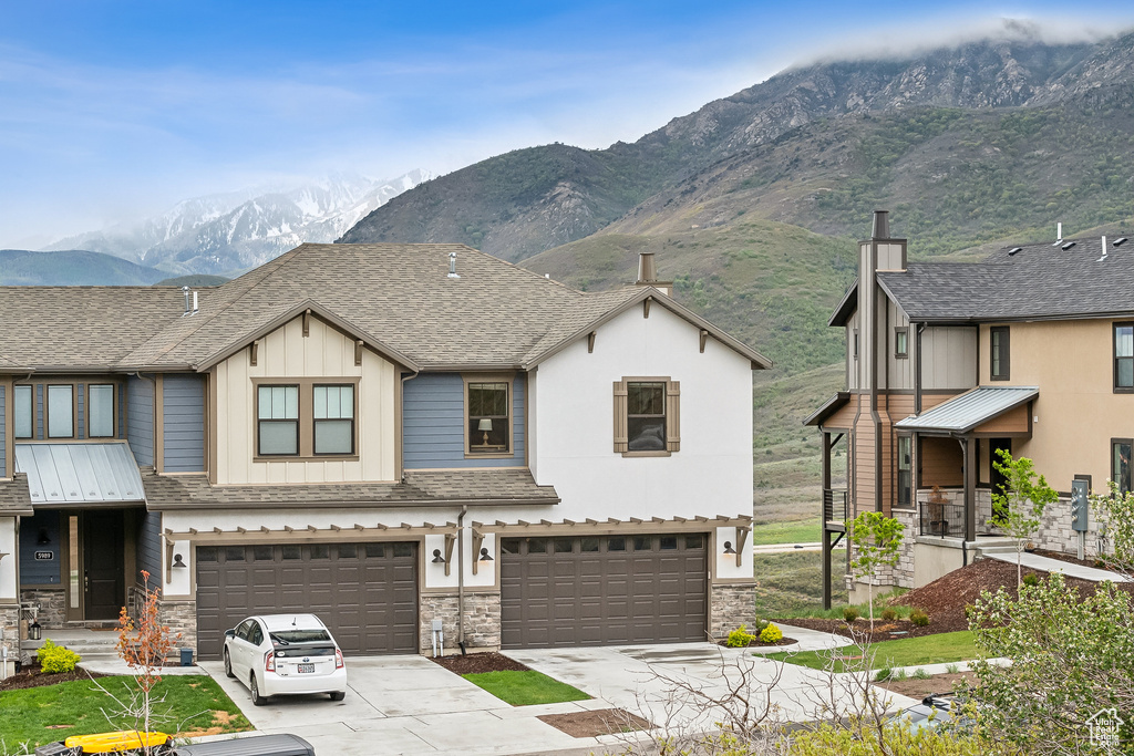 Multi unit property featuring a mountain view, stone siding, an attached garage, concrete driveway, and board and batten siding
