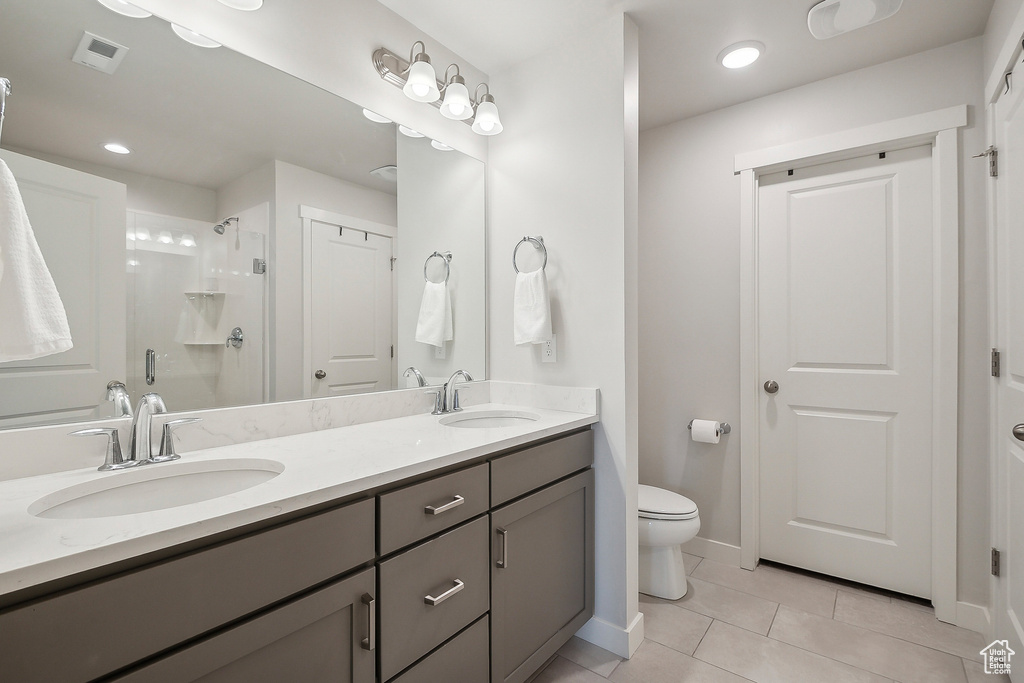 Bathroom featuring tile patterned flooring, a stall shower, toilet, double vanity, and baseboards