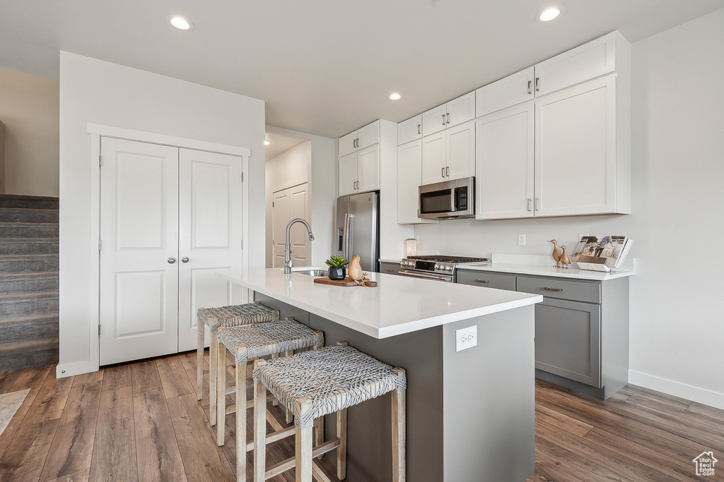 Kitchen with appliances with stainless steel finishes, wood finished floors, an island with sink, baseboards, and a breakfast bar area
