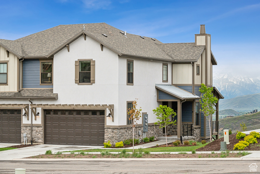 View of front of house featuring a mountain view, stone siding, a chimney, and a garage