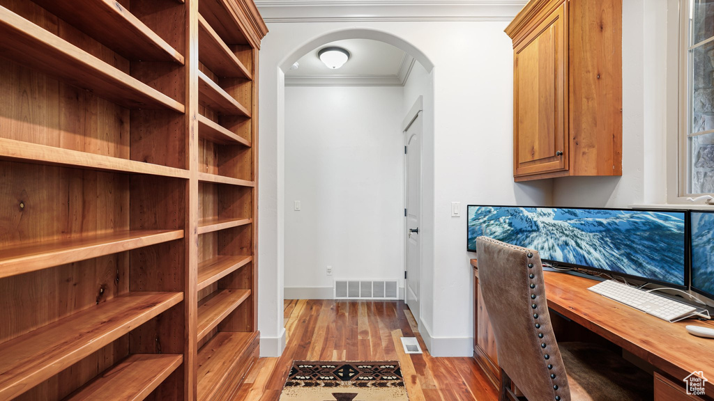 Office area featuring ornamental molding, arched walkways, light wood-style flooring, and baseboards