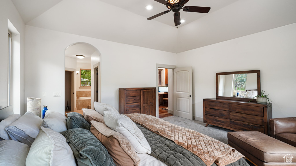 Bedroom featuring arched walkways, multiple windows, light carpet, and connected bathroom