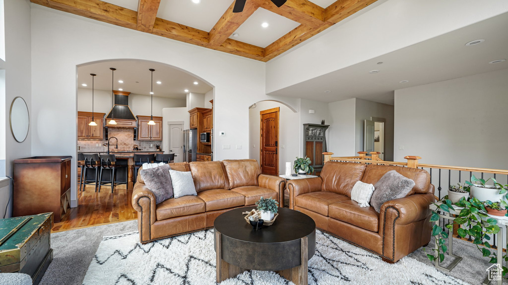 Living room featuring arched walkways, a high ceiling, coffered ceiling, beam ceiling, and light wood-type flooring