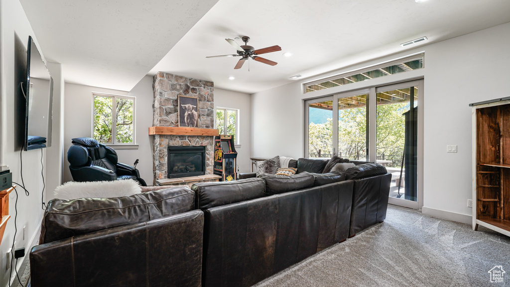 Living room featuring a stone fireplace, a ceiling fan, light colored carpet, baseboards, and recessed lighting