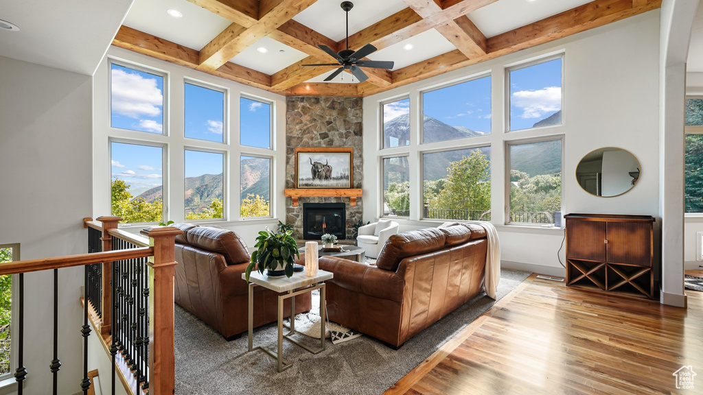 Living room featuring wood finished floors, a high ceiling, a ceiling fan, a fireplace, and beamed ceiling