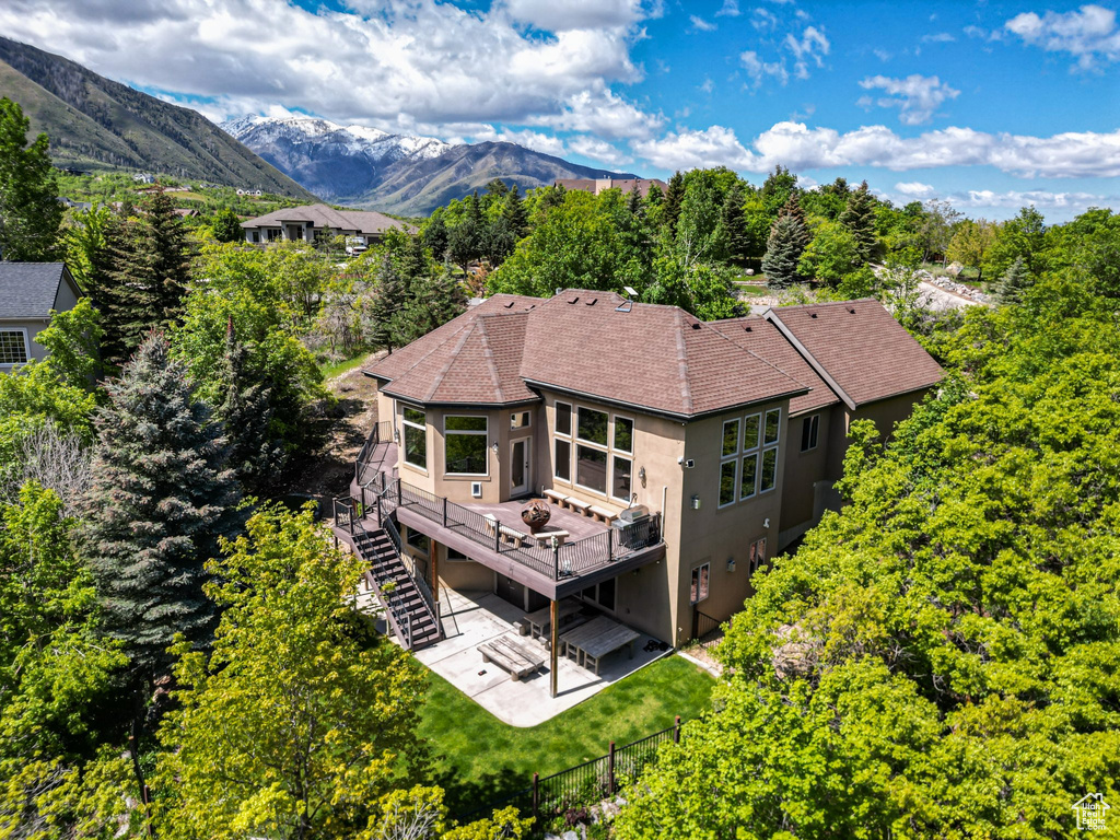 Rear view of property featuring stairway, stucco siding, a deck with mountain view, a patio area, and a lawn