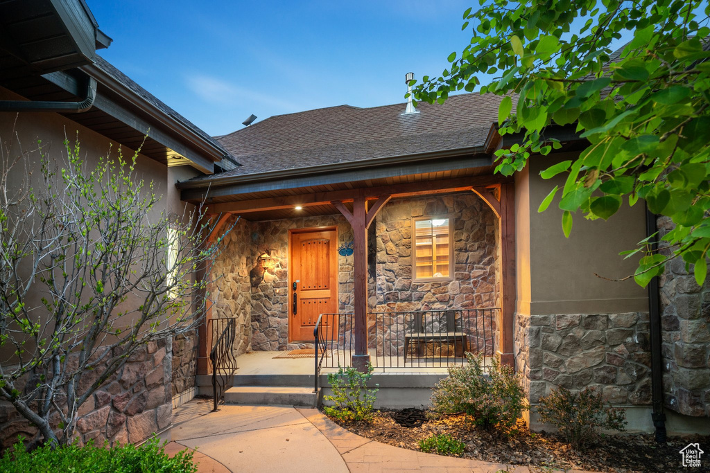 Entrance to property with stone siding, stucco siding, covered porch, and roof with shingles