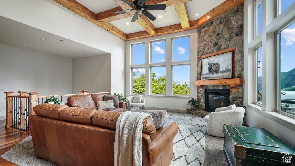 Living room featuring healthy amount of natural light, a fireplace, a ceiling fan, beam ceiling, and a towering ceiling