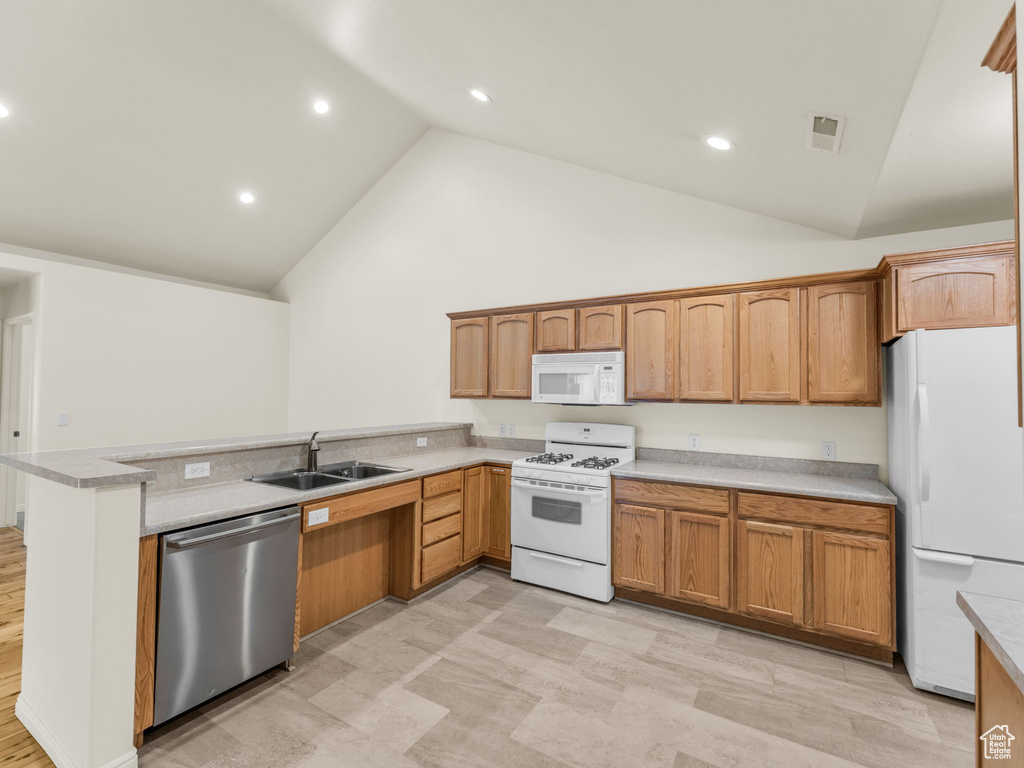 Kitchen with white appliances, a sink, a peninsula, light countertops, and recessed lighting