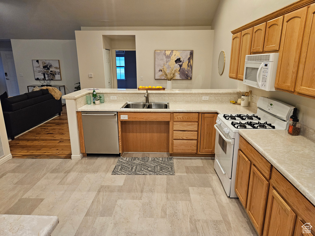 Kitchen with white appliances, a peninsula, light countertops, light wood-style flooring, and open floor plan