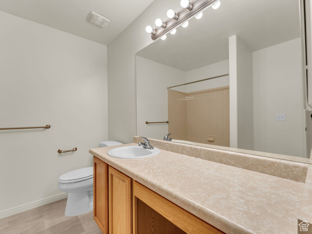 Bathroom with toilet, baseboards, a shower, vanity, and wood finished floors