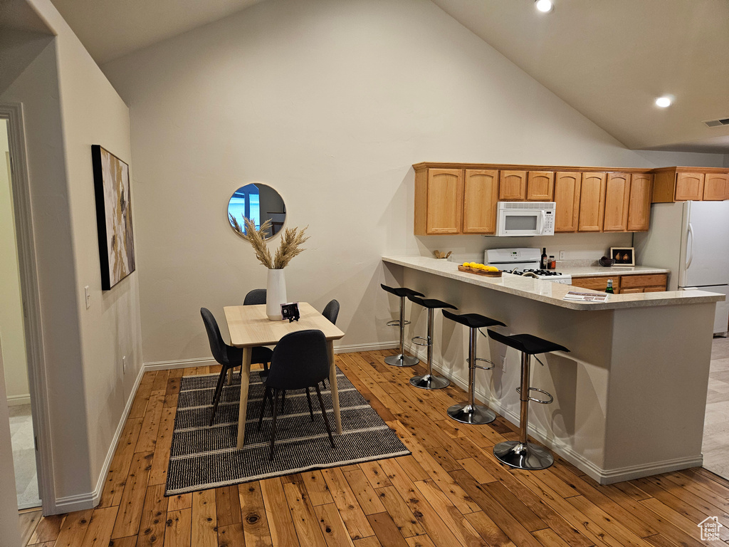 Kitchen featuring white appliances, high vaulted ceiling, light wood-type flooring, a peninsula, and a breakfast bar
