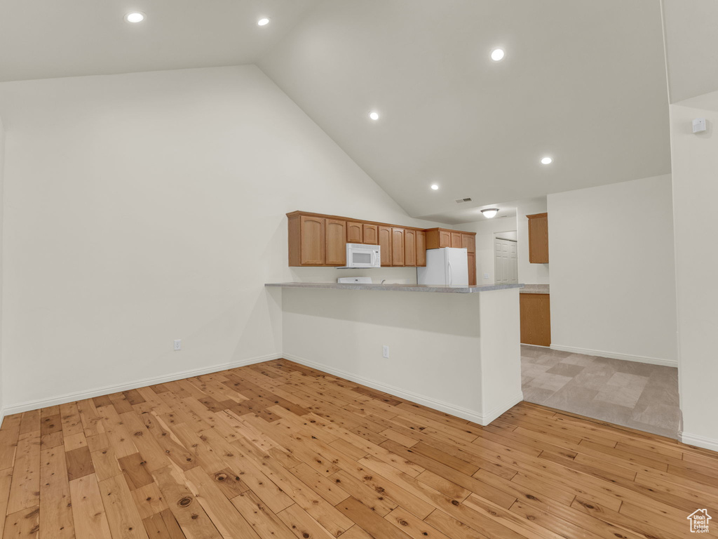 Kitchen with white appliances, light wood-style floors, a peninsula, recessed lighting, and high vaulted ceiling