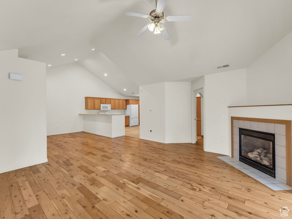 Unfurnished living room with recessed lighting, light wood-style floors, a fireplace, lofted ceiling, and arched walkways