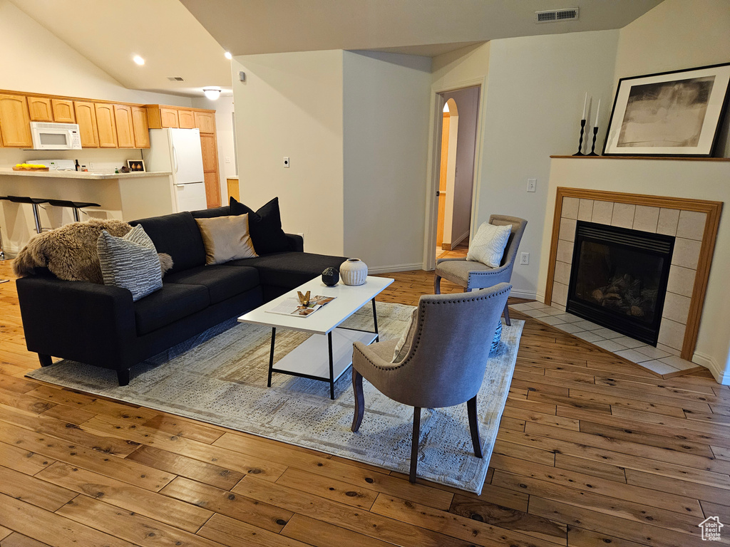 Living room featuring wood-type flooring, lofted ceiling, a tiled fireplace, and recessed lighting