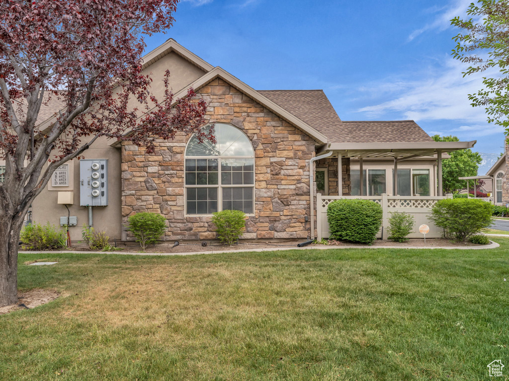 View of front facade with stone siding, a front yard, and a shingled roof