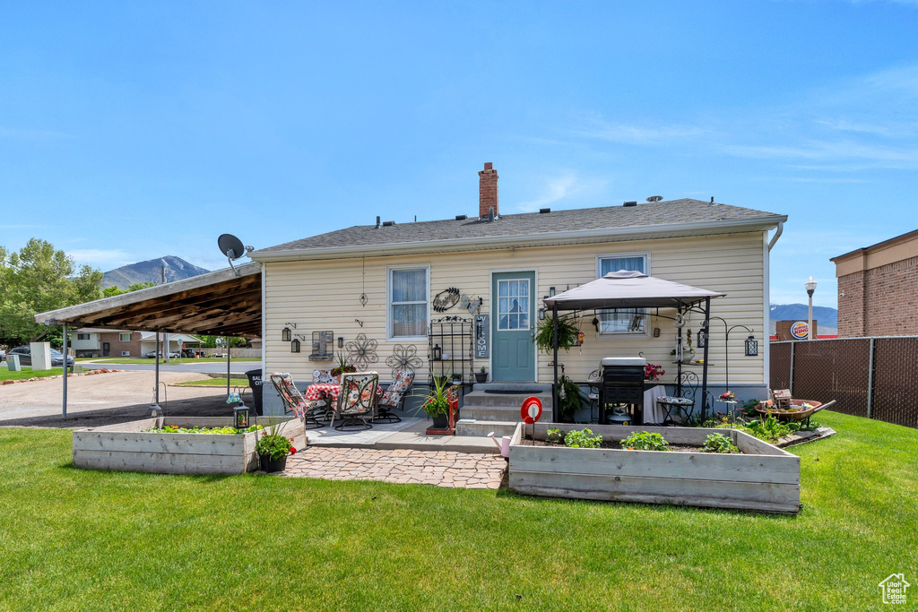 Rear view of property featuring a vegetable garden, a patio, a chimney, and a carport