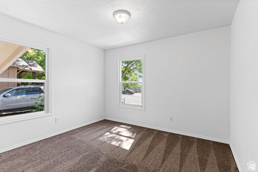 Spare room with dark carpet, healthy amount of natural light, baseboards, and a textured ceiling