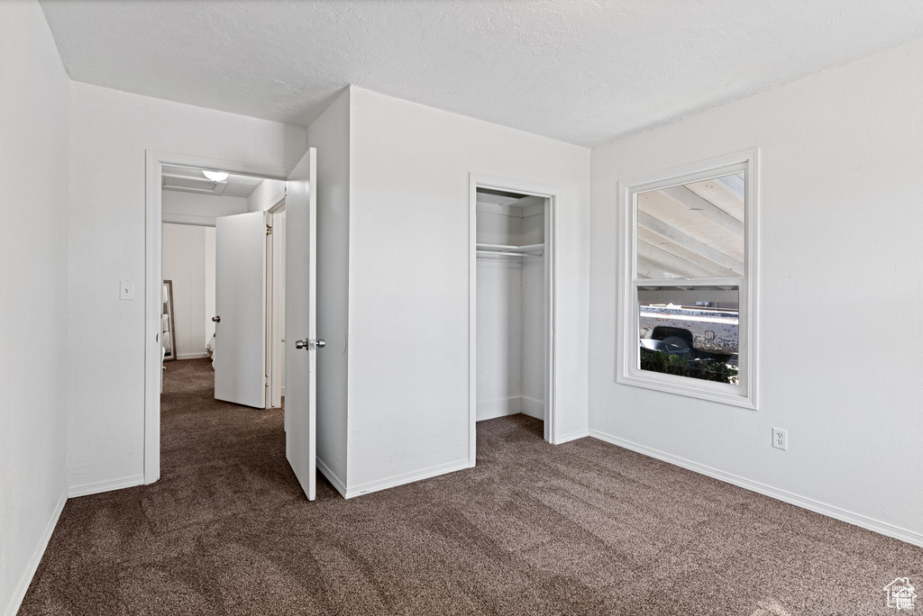 Unfurnished bedroom with dark colored carpet, baseboards, and a closet