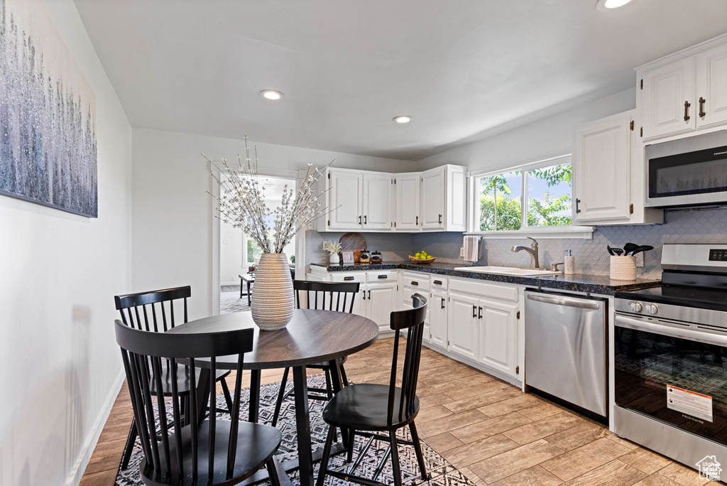 Kitchen featuring appliances with stainless steel finishes, dark countertops, a sink, tasteful backsplash, and white cabinets