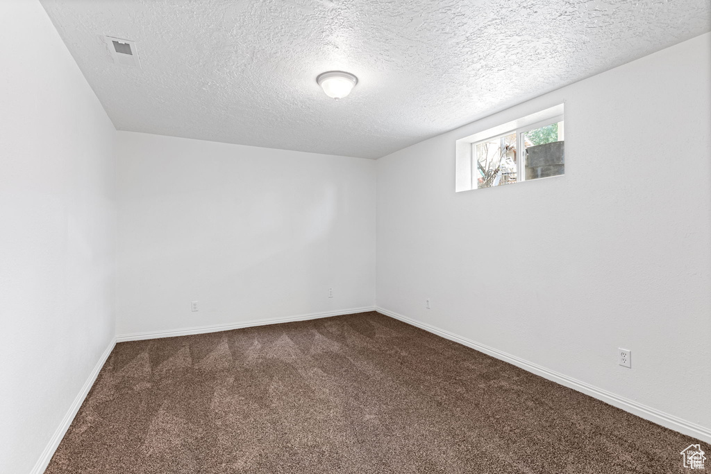 Empty room with dark colored carpet, a textured ceiling, and baseboards