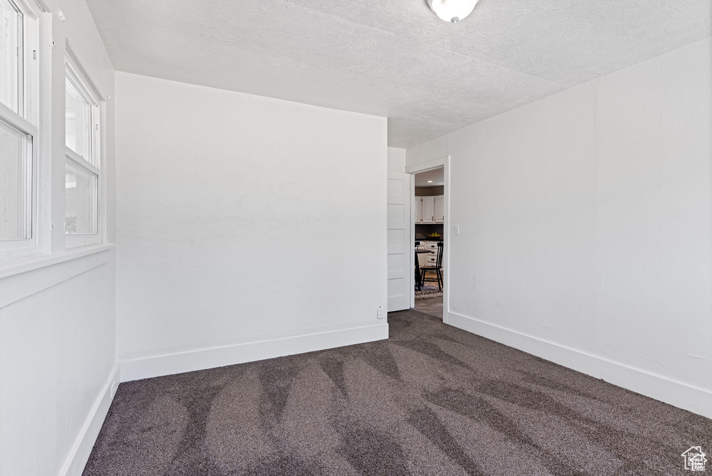 Empty room with dark colored carpet, a textured ceiling, and baseboards