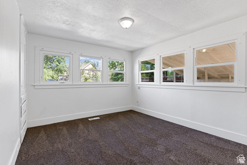 Spare room with a textured ceiling, baseboards, and dark colored carpet
