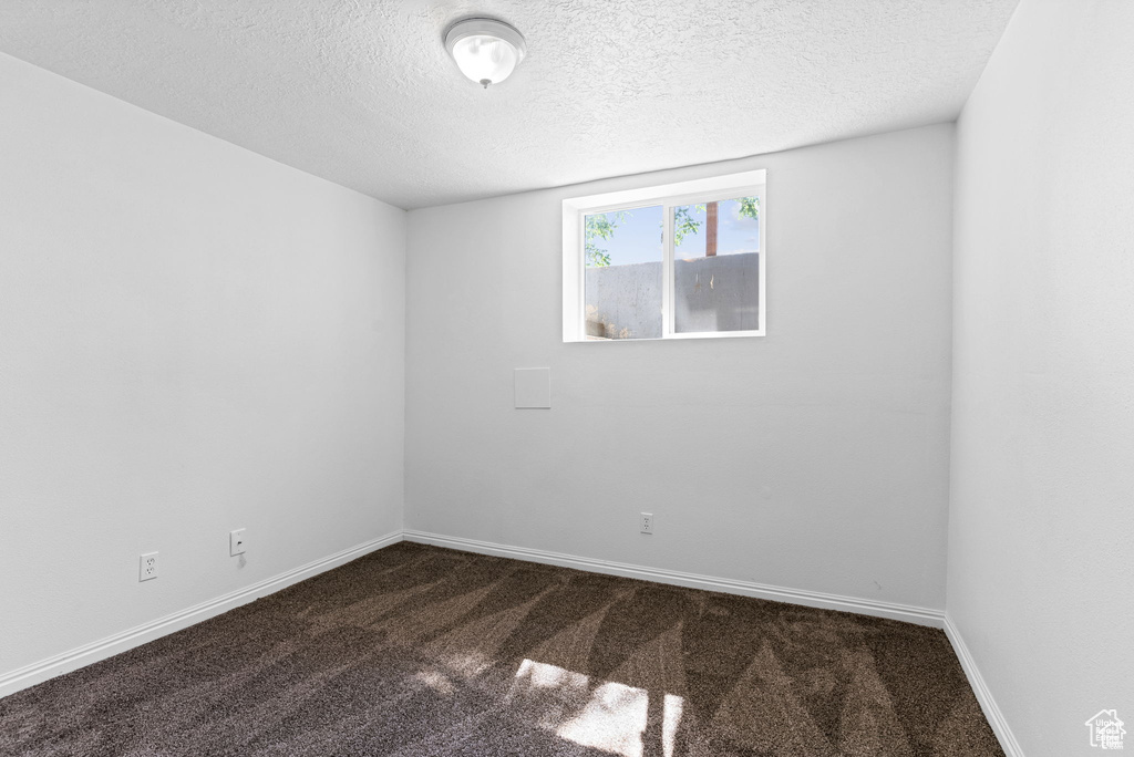 Unfurnished room featuring a textured ceiling, dark carpet, and baseboards