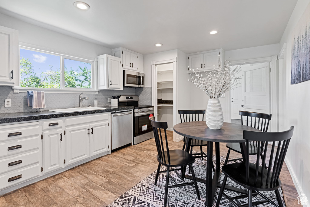 Kitchen with appliances with stainless steel finishes, a sink, dark countertops, white cabinets, and recessed lighting