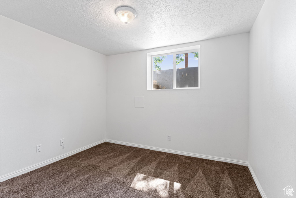 Empty room with dark colored carpet, a textured ceiling, and baseboards