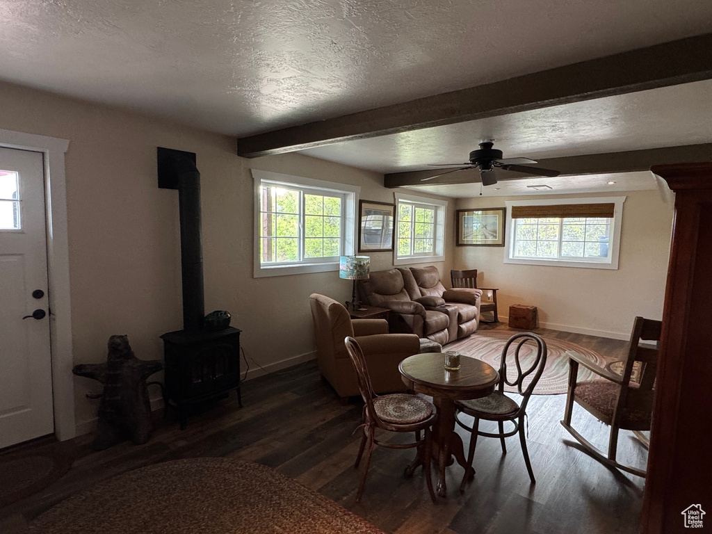 Dining room featuring a wood stove, baseboards, wood finished floors, beam ceiling, and a textured ceiling