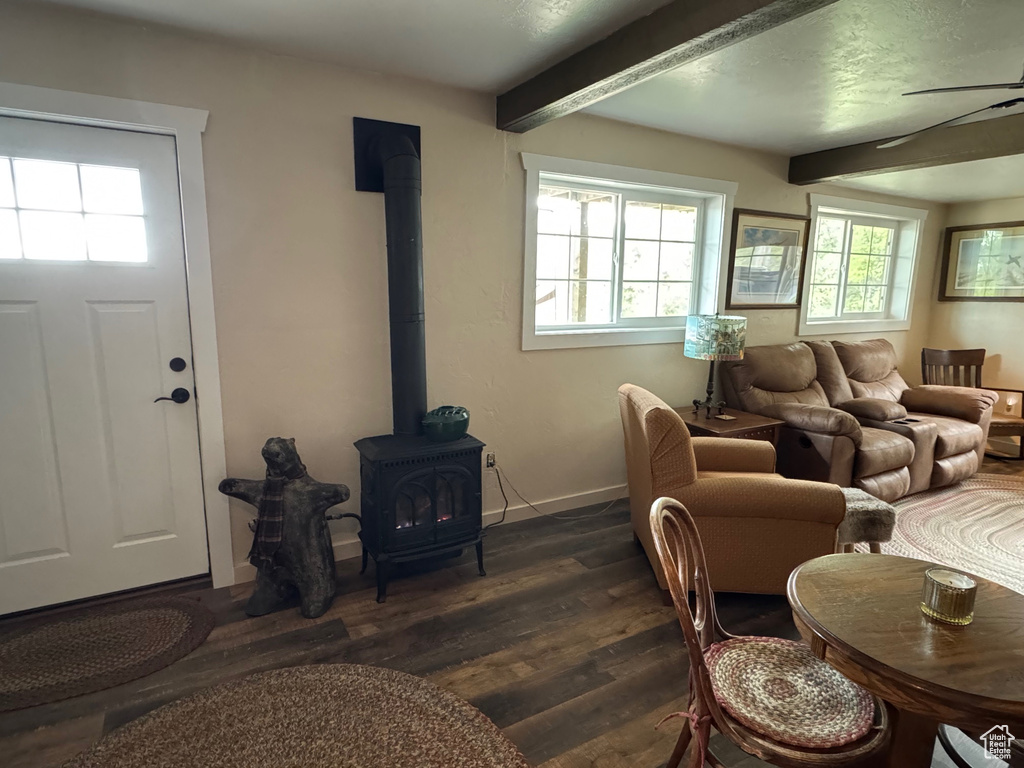 Living area featuring a wood stove, beamed ceiling, dark wood-style floors, and baseboards
