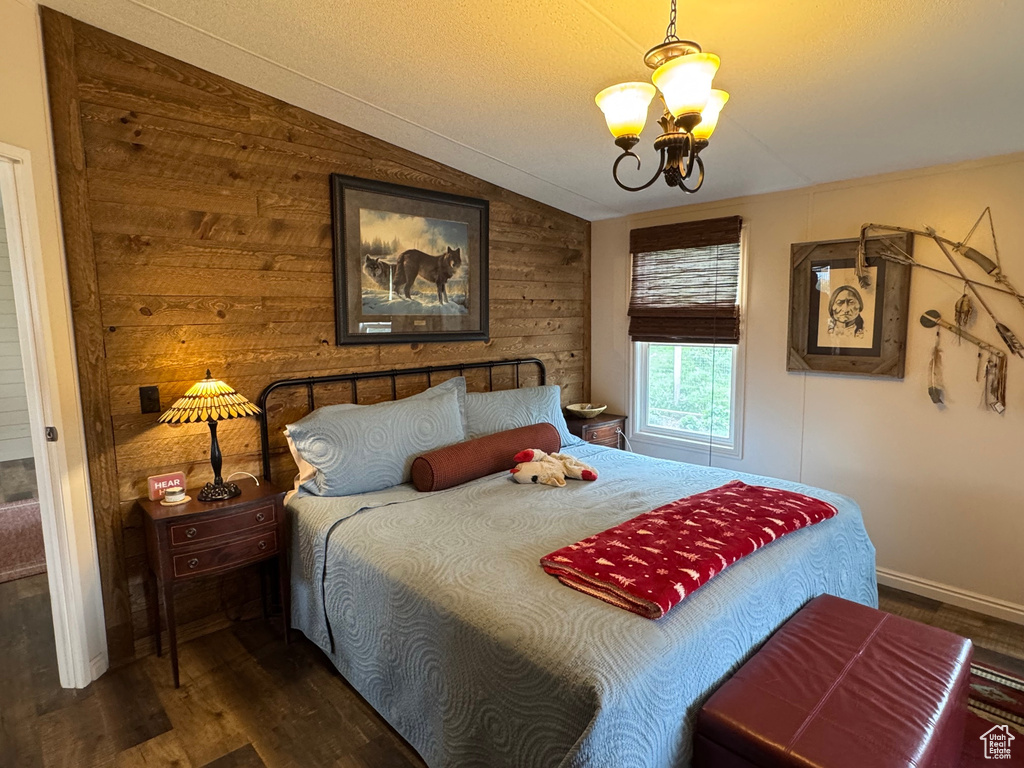 Bedroom with a chandelier, dark wood-type flooring, vaulted ceiling, wooden walls, and baseboards