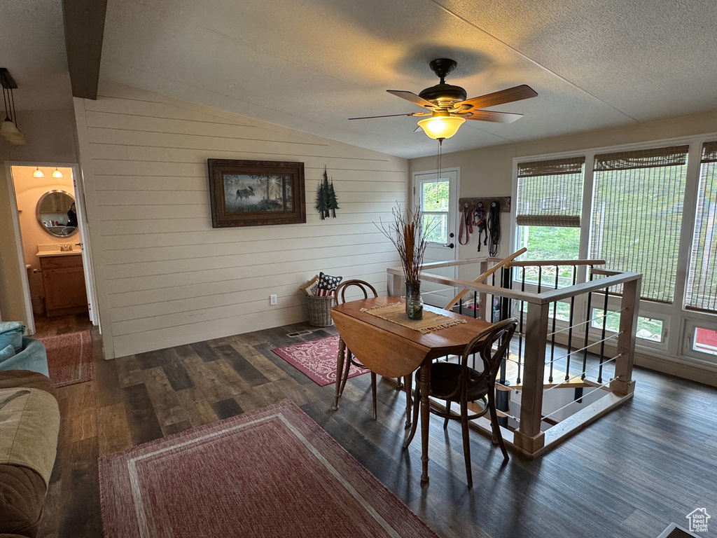 Dining room featuring wood finished floors, ceiling fan, lofted ceiling, a textured ceiling, and wood walls