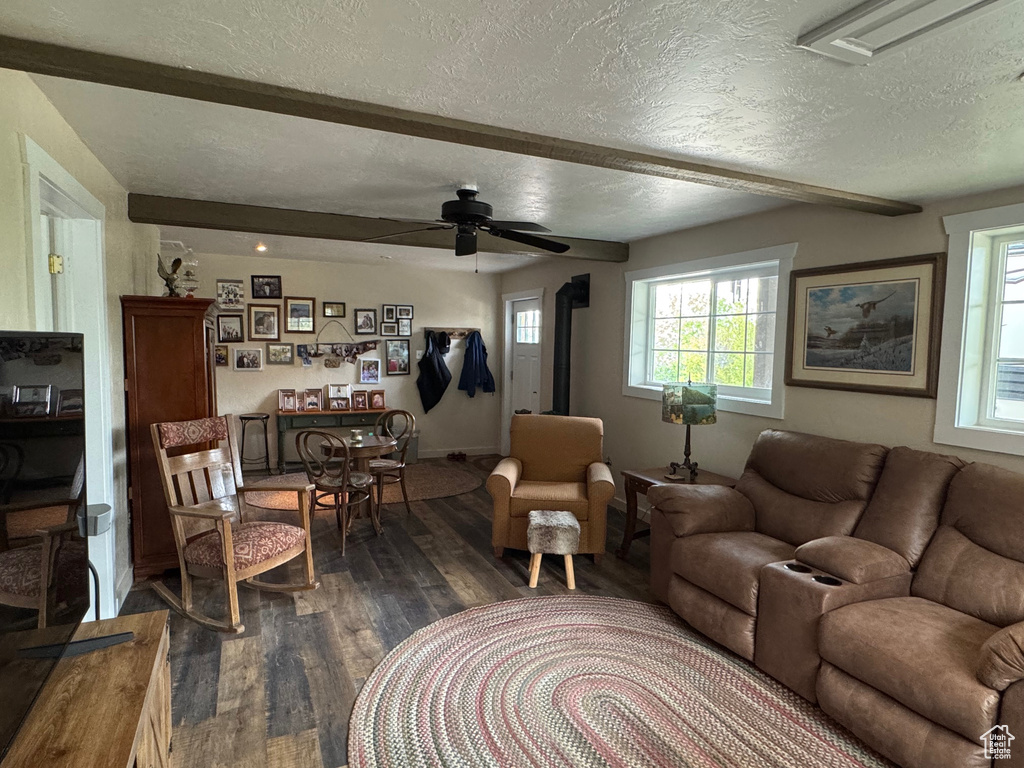 Living area featuring a textured ceiling, dark wood-type flooring, beamed ceiling, healthy amount of natural light, and a ceiling fan