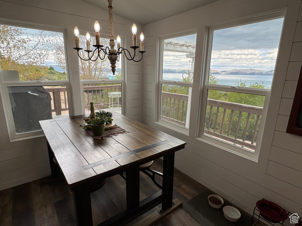 Dining space featuring dark wood-style floors, a chandelier, a water view, vaulted ceiling, and wooden walls