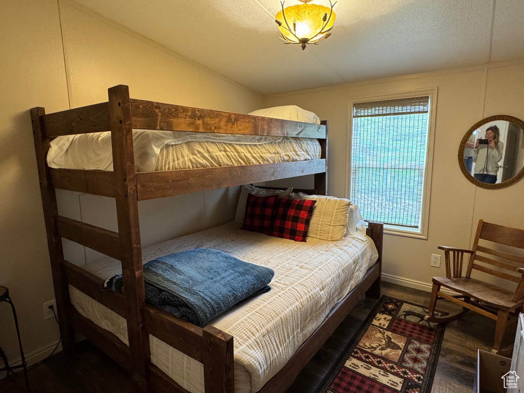 Bedroom with wood finished floors, baseboards, vaulted ceiling, and a textured ceiling