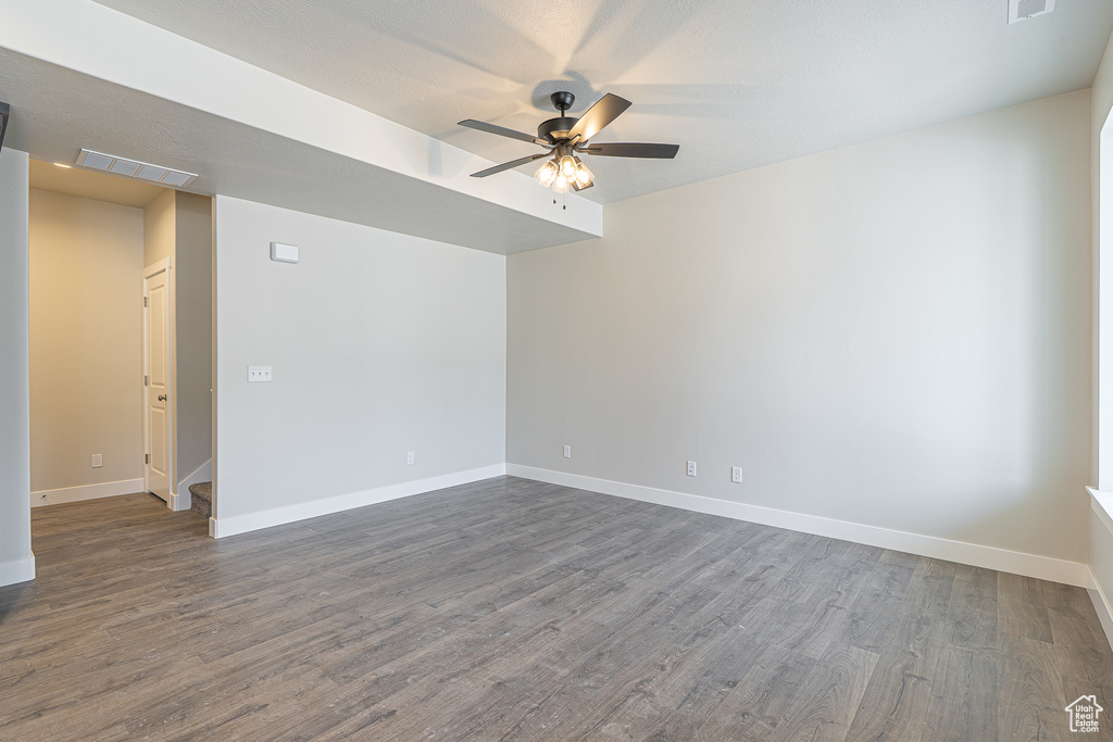Empty room featuring dark wood-type flooring, a ceiling fan, and baseboards