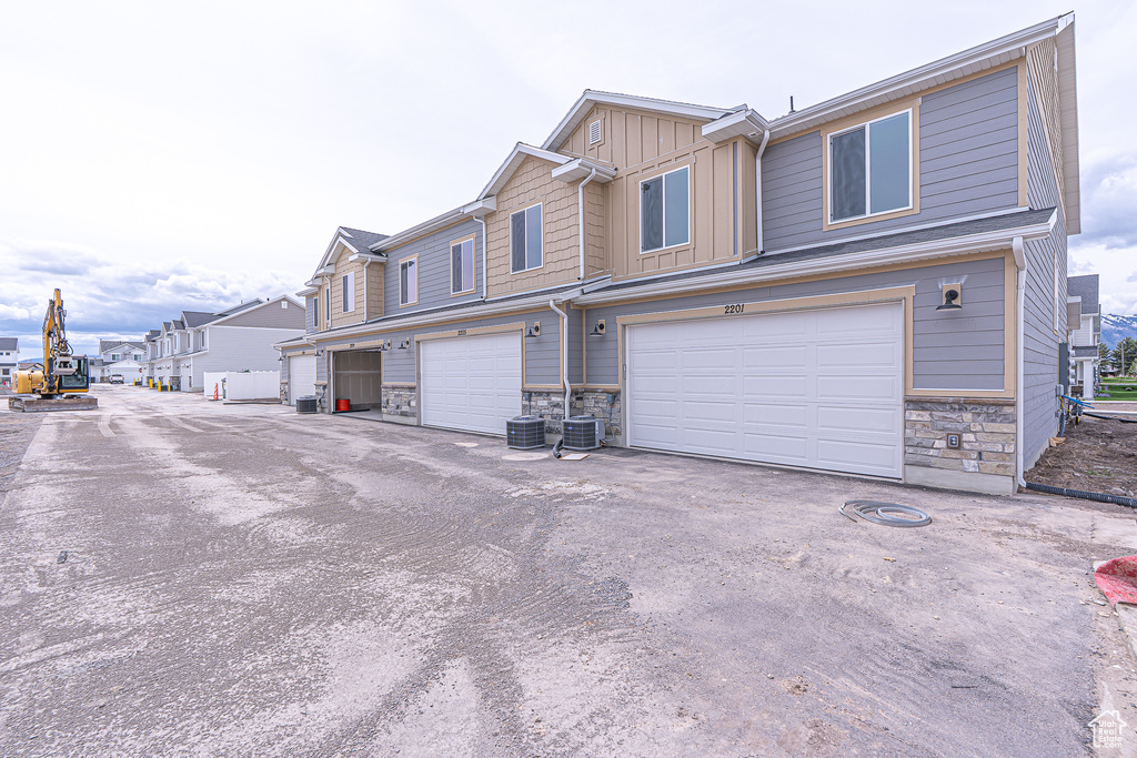View of side of home with stone siding, board and batten siding, central AC unit, and an attached garage
