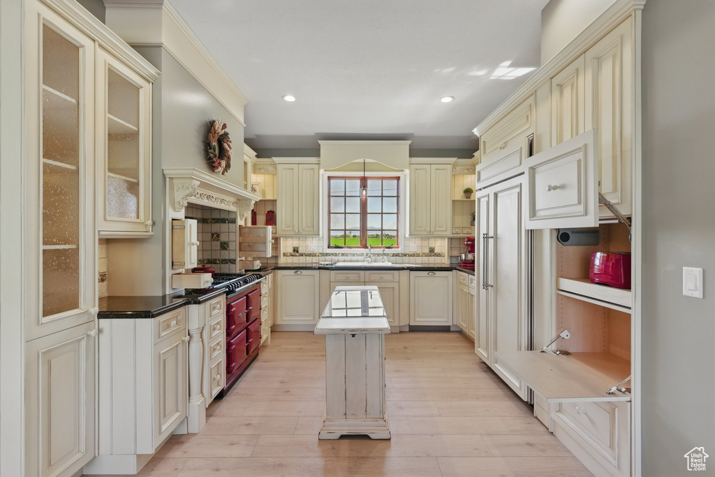 Kitchen with light wood-style flooring, cream cabinetry, dark countertops, and tasteful backsplash