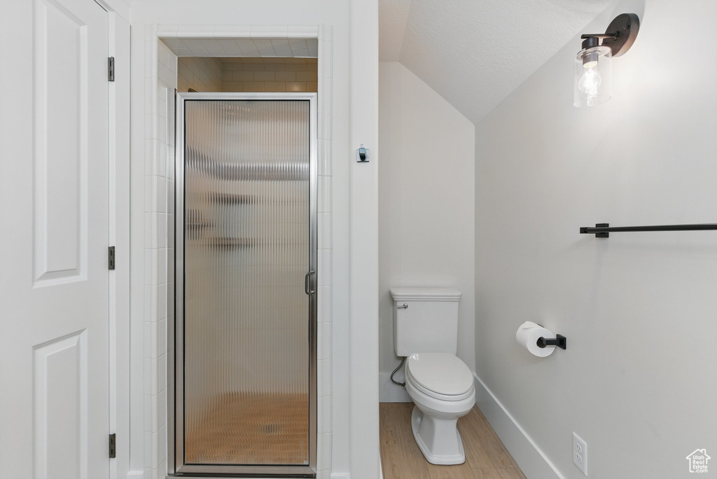 Full bath featuring toilet, wood finished floors, a stall shower, baseboards, and vaulted ceiling