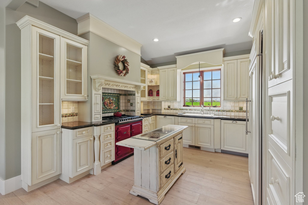 Kitchen with light wood finished floors, a sink, cream cabinetry, backsplash, and black electric stovetop